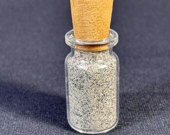 Puede incluir: Un frasco de vidrio transparente con tapa de madera lleno de granos de pimienta negra.