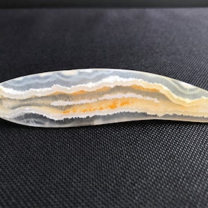 May include: A polished, white agate slice with a curved shape and a banded pattern of white and orange.