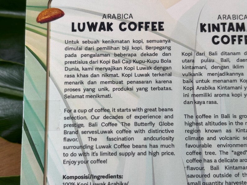 Puede incluir: Primer plano de una etiqueta impresa en blanco y verde con texto sobre el caf&eacute; Luwak y el caf&eacute; Kintamani. La etiqueta incluye las palabras "ARABICA" y "LUWAK COFFEE". El texto describe el origen y el sabor del caf&eacute;.