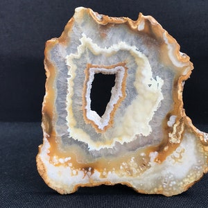 May include: A large, irregularly shaped agate slice with a hole in the center. The agate is white with brown and yellow banding.