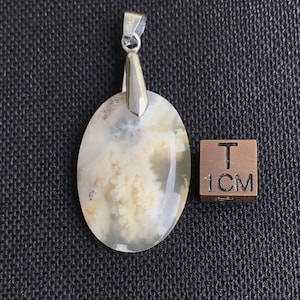 May include: An oval pendant with a silver bail and a natural stone. The stone has a cloudy, cream-colored pattern with hints of gray. A 1 cm cube is next to the pendant for size reference.