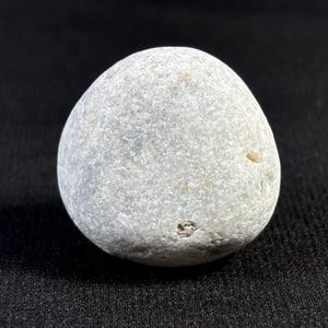 May include: A smooth, round, light gray stone with small, light brown flecks.