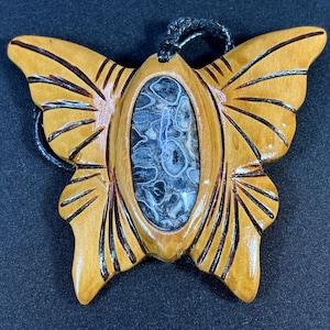 以下が含まれることがあります： 彫刻されたデザインと中央に黒と白の瑪瑙石が埋め込まれた木製の蝶のペンダント