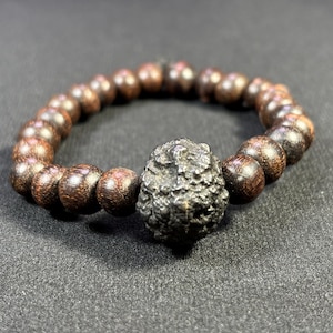 以下が含まれることがあります： 濃い茶色の木製ビーズブレスレットで、中央に黒い金属ビーズが付いています。