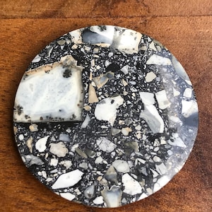 May include: A round, black and white agate coaster with a speckled pattern. The coaster is made of natural stone and has a smooth, polished surface.