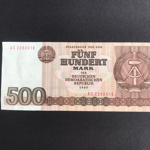 May include: A 500 Mark banknote from the German Democratic Republic, dated 1985. The note features a red and brown design with the text "F&uuml;nf Hundert Mark" and a compass and hammer symbol.