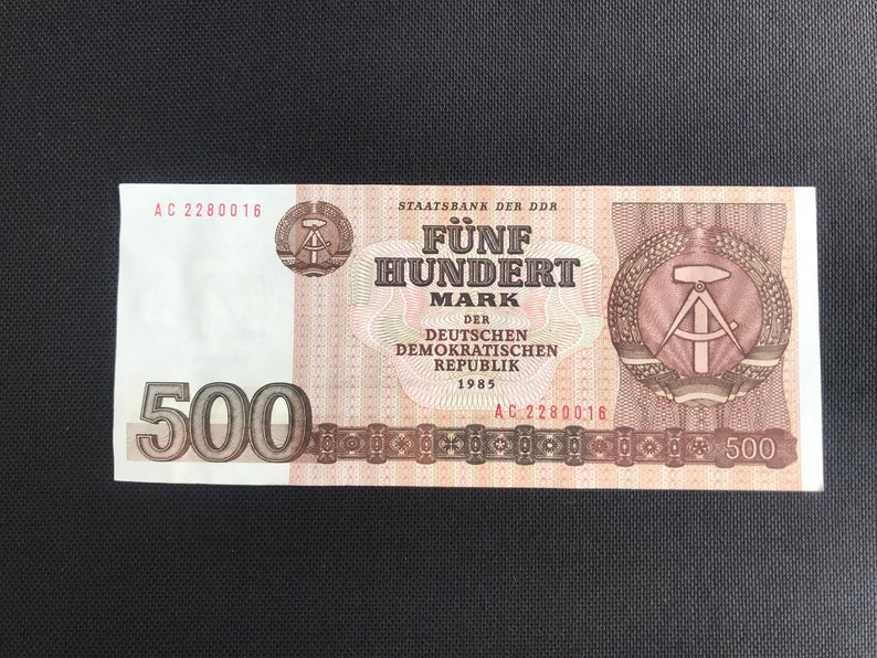 May include: A 500 Mark banknote from the German Democratic Republic, dated 1985. The note features a red and brown design with the text "F&uuml;nf Hundert Mark" and a compass and hammer symbol.