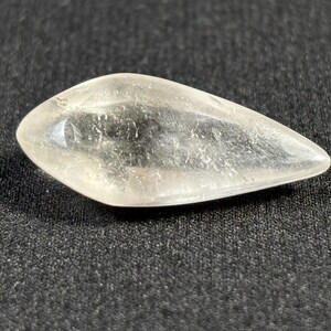 May include: A clear, faceted, teardrop-shaped crystal with a pointed tip. The crystal has a slightly cloudy appearance.