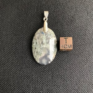 May include: A green and white agate pendant with a silver bail. The pendant is oval shaped and measures approximately 1 inch in length.
