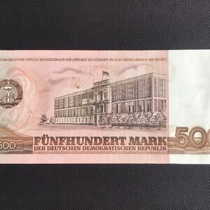May include: A 500 Mark banknote from the German Democratic Republic. The banknote features a building with a flag on top and the text "F&Uuml;NFHUNDERT MARK DER DEUTSCHEN DEMOKRATISCHEN REPUBLIK".