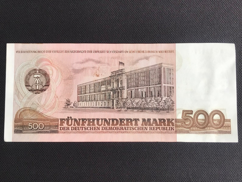 May include: A 500 Mark banknote from the German Democratic Republic. The banknote features a building with a flag on top and the text "F&Uuml;NFHUNDERT MARK DER DEUTSCHEN DEMOKRATISCHEN REPUBLIK".
