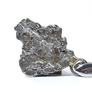 May include: A close-up of a silver-coloured meteorite with a rough, uneven surface. The meteorite is mounted on a metal stand.
