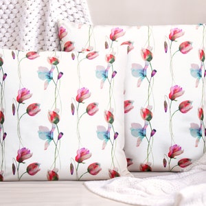 Pode incluir: Duas capas de almofada brancas com um padr&atilde;o floral de aquarela. O padr&atilde;o apresenta flores rosa, vermelhas e azuis com caules verdes sobre um fundo branco.