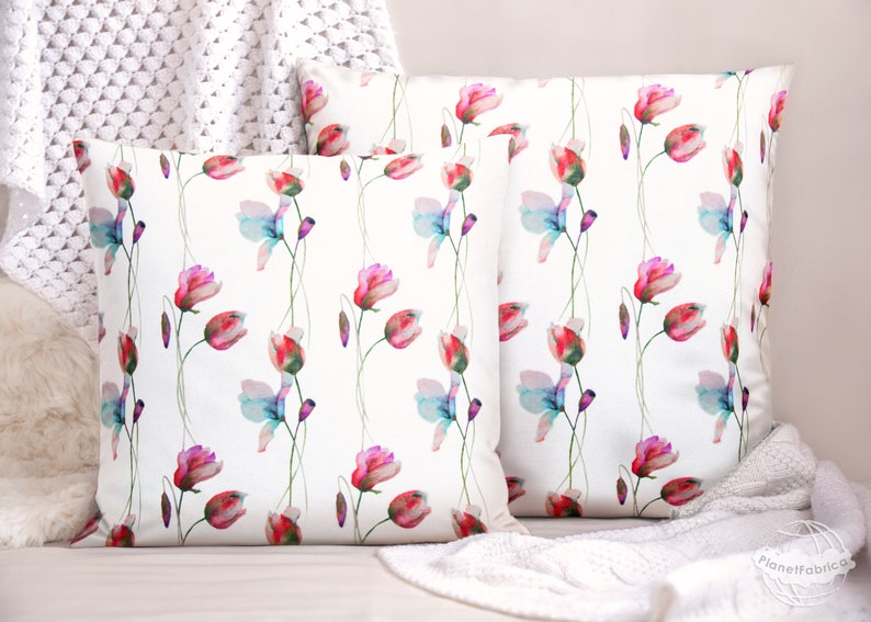 Pode incluir: Duas capas de almofada brancas com um padr&atilde;o floral de aquarela. O padr&atilde;o apresenta flores rosa, vermelhas e azuis com caules verdes sobre um fundo branco.