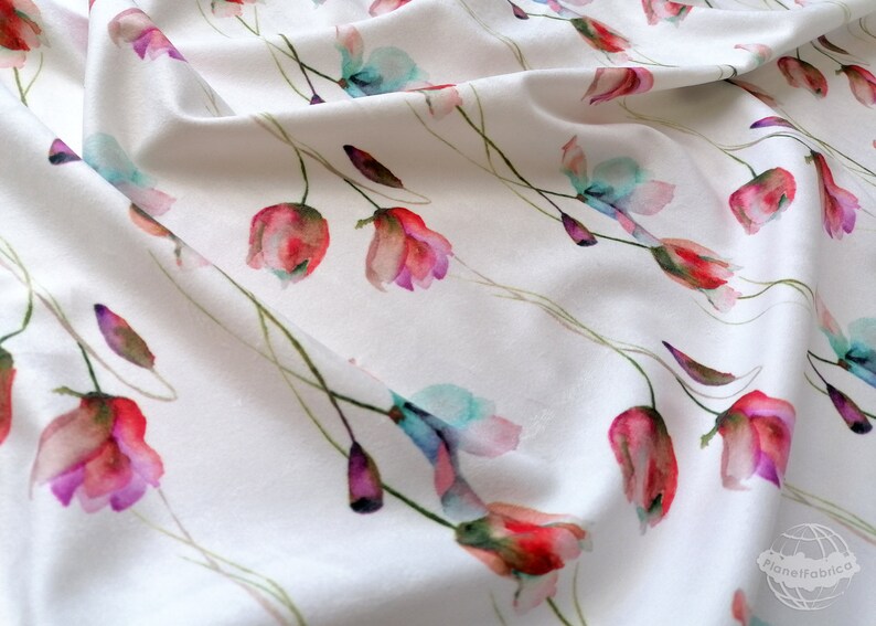 Pode incluir: Tecido branco com estampa floral em aquarela com flores rosa, vermelhas e azuis. As flores est&atilde;o dispostas em um padr&atilde;o repetitivo no tecido.