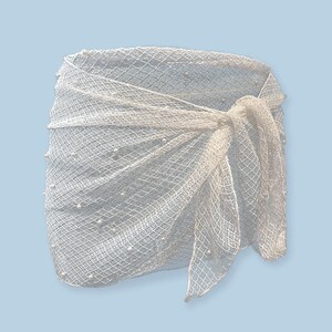 May include: White crochet wrap skirt with a beaded design. The skirt is tied at the waist with a bow.