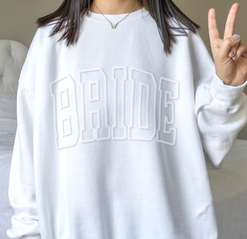 May include: White sweatshirt with the word "BRIDE" in large, raised, white letters.