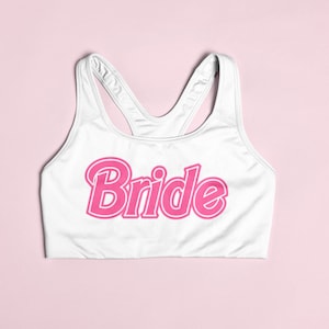 May include: White sports bra with the word "Bride" in pink outlined letters.