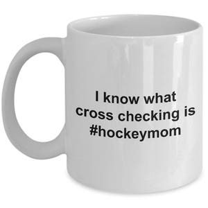 Może przedstawiać: Biały ceramiczny kubek do kawy z czarnym tekstem, kt&oacute;ry brzmi "Wiem, co to jest cross-checking #hockeymom"