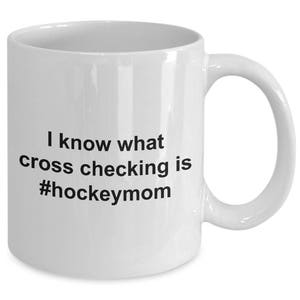 Może przedstawiać: Biały ceramiczny kubek do kawy z czarnym tekstem, kt&oacute;ry brzmi "Wiem, co to jest cross-checking #hockeymom"