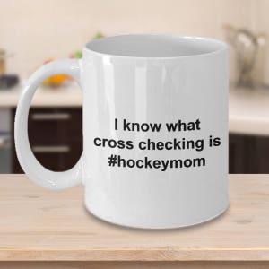 Może przedstawiać: Biały ceramiczny kubek do kawy z czarnym tekstem, kt&oacute;ry brzmi "Wiem, co to jest cross-checking #hockeymom"
