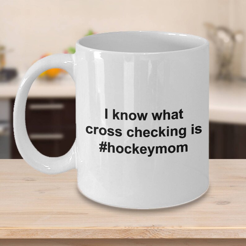 Może przedstawiać: Biały ceramiczny kubek do kawy z czarnym tekstem, kt&oacute;ry brzmi "Wiem, co to jest cross-checking #hockeymom"