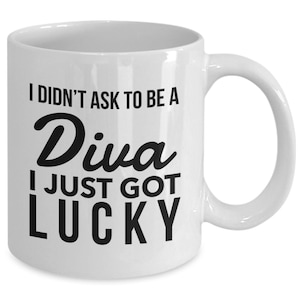 May include: White ceramic coffee mug with black text that reads "I didn't ask to be a Diva I just got lucky".
