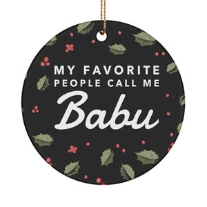May include: A round Christmas ornament with a black background and a white holly leaf pattern. The ornament has the text "My favorite people call me Babu" in white.
