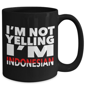 May include: Black coffee mug with white text that reads "I'm not yelling I'm Indonesian" with a red and white stripe across the word "Indonesian".