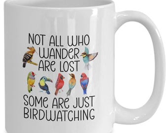 May include: White ceramic coffee mug with a black and white design that says "Not all who wander are lost, some are just birdwatching". The design includes colorful illustrations of various birds.