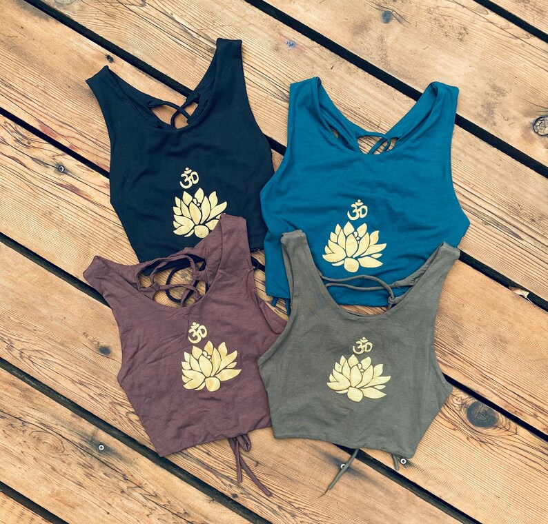 May include: Four tank tops with a gold lotus flower and Om symbol design. The tank tops are in black, teal, brown, and olive green.