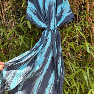 Peut inclure: Une robe longue portefeuille avec une taille nou&eacute;e et des manches courtes, orn&eacute;e d'un motif tie-dye audacieux en gris anthracite fonc&eacute; et bleu turquoise vif. Le v&ecirc;tement comprend un cintre noir et une &eacute;tiquette indiquant Prema au col.
