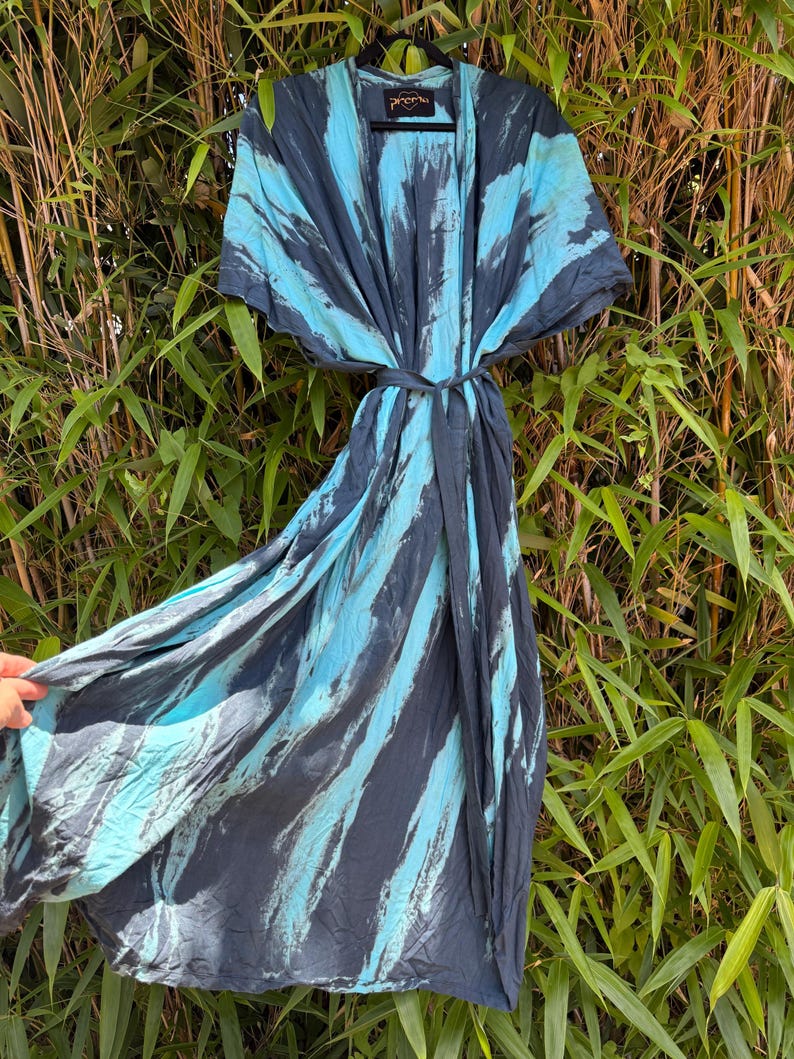 Peut inclure: Une robe longue portefeuille avec une taille nou&eacute;e et des manches courtes, orn&eacute;e d'un motif tie-dye audacieux en gris anthracite fonc&eacute; et bleu turquoise vif. Le v&ecirc;tement comprend un cintre noir et une &eacute;tiquette indiquant Prema au col.