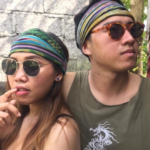 May include: Two people wearing headbands with colorful patterns and sunglasses. The person on the right is wearing a green tank top with a white dragon design.