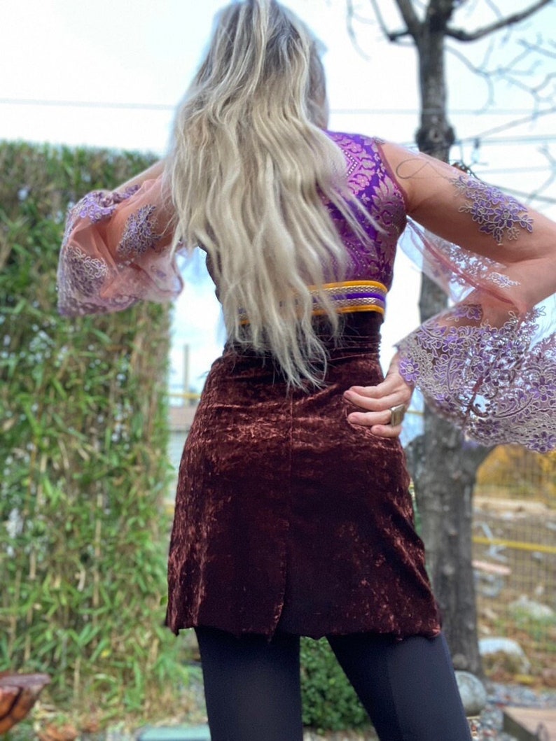 May include: A brown velvet skirt with a high waist and a fitted silhouette. The skirt is paired with a purple and gold brocade top with sheer lace sleeves.