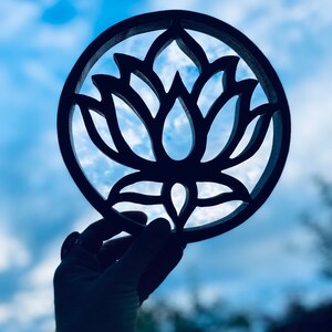 May include: A black wooden cutout of a lotus flower, held up against a blue sky with white clouds.