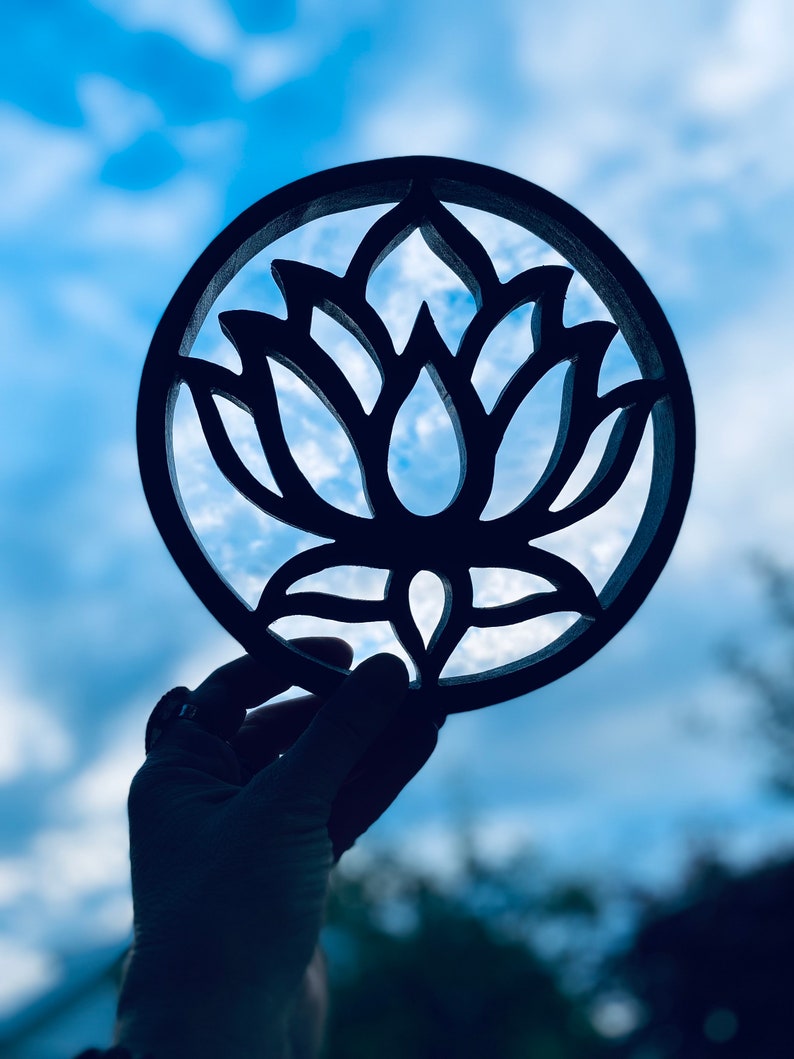 May include: A black wooden cutout of a lotus flower, held up against a blue sky with white clouds.