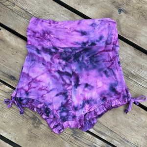 Puede incluir: Shorts de color morado tie-dye con un dobladillo con volantes y cordones de ajuste en los lados.