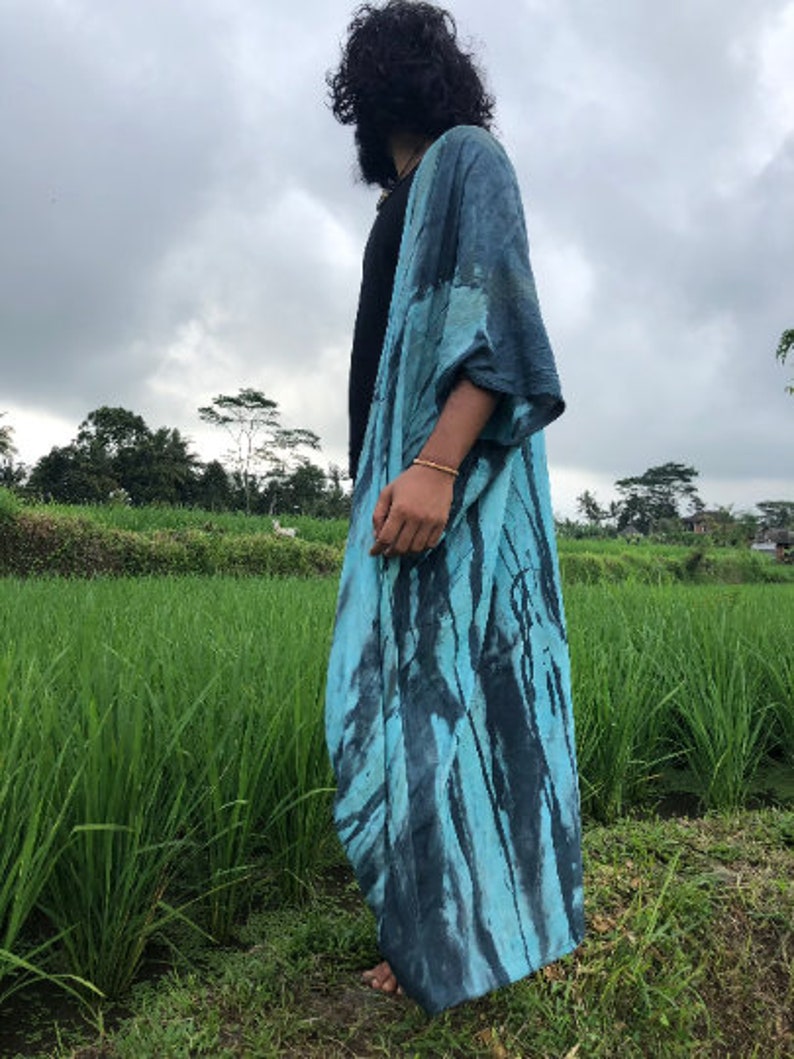 Peut inclure: Un long kimono ouvert sur le devant arborant un motif tie-dye aux nuances de turquoise vif et de noir charbon profond. Le v&ecirc;tement pr&eacute;sente des manches larges et amples ainsi qu'une silhouette fluide tombant jusqu'au sol.