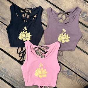 May include: Three tank tops with a lotus flower and Om symbol design. The tank tops are black, brown, and pink. The lotus flower and Om symbol are gold.