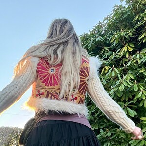K&ouml;nnte beinhalten: Ein cremefarbener Pullover mit einem dekorativen R&uuml;ckenteil mit einem floralen Design in Rosa-, Gold- und Rott&ouml;nen. Der Pullover hat lange &Auml;rmel und einen Kunstfellbesatz am Bund.