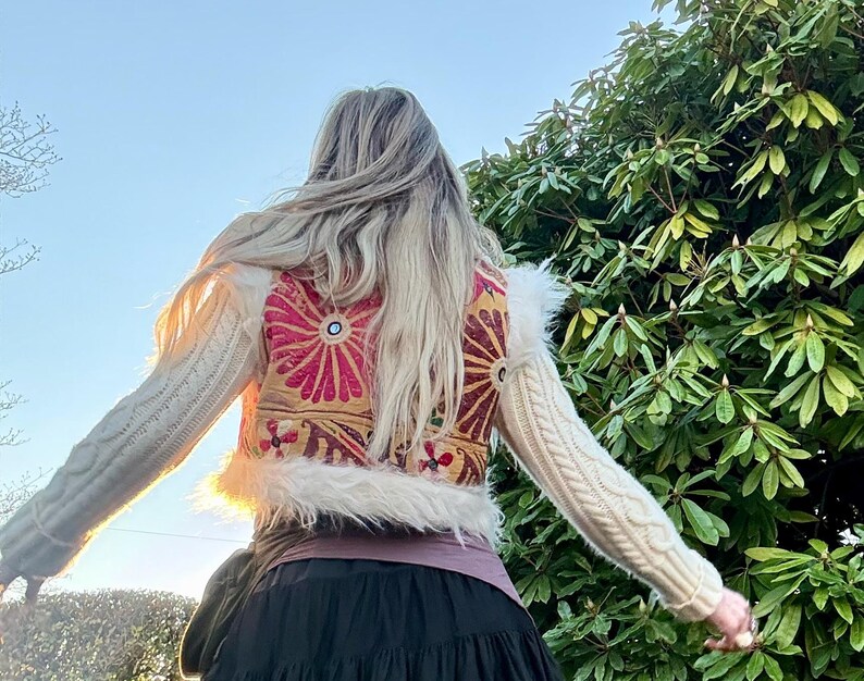 K&ouml;nnte beinhalten: Ein cremefarbener Pullover mit einem dekorativen R&uuml;ckenteil mit einem floralen Design in Rosa-, Gold- und Rott&ouml;nen. Der Pullover hat lange &Auml;rmel und einen Kunstfellbesatz am Bund.