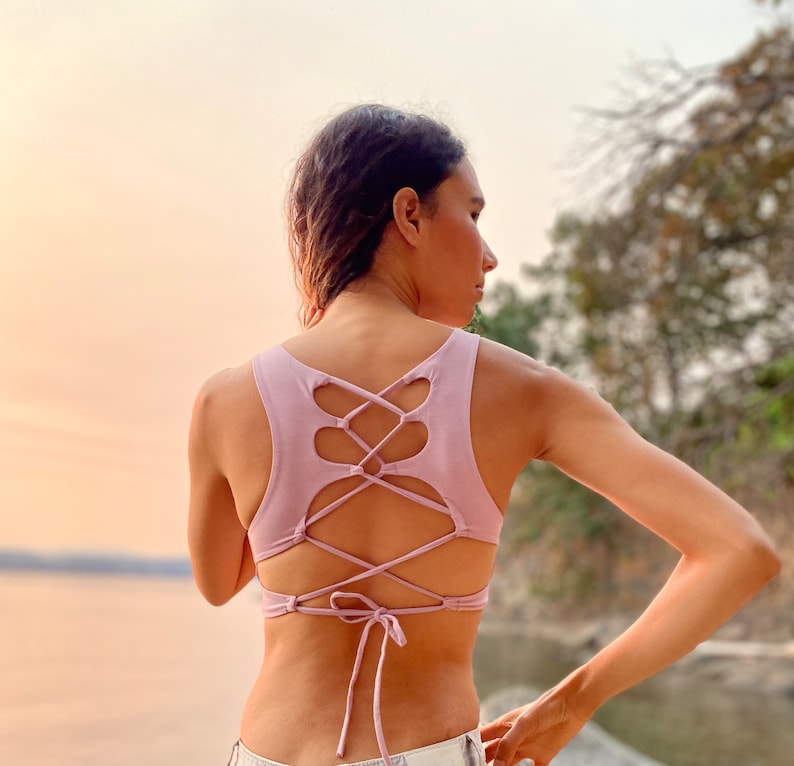 May include: A light purple tank top with a criss-cross lace-up back design. The top is made of a soft, stretchy fabric and has a relaxed fit.