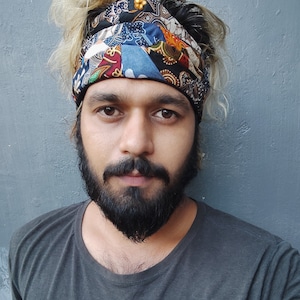 May include: A man with blonde hair and a beard is wearing a colorful patterned headband. He is wearing a dark grey t-shirt.