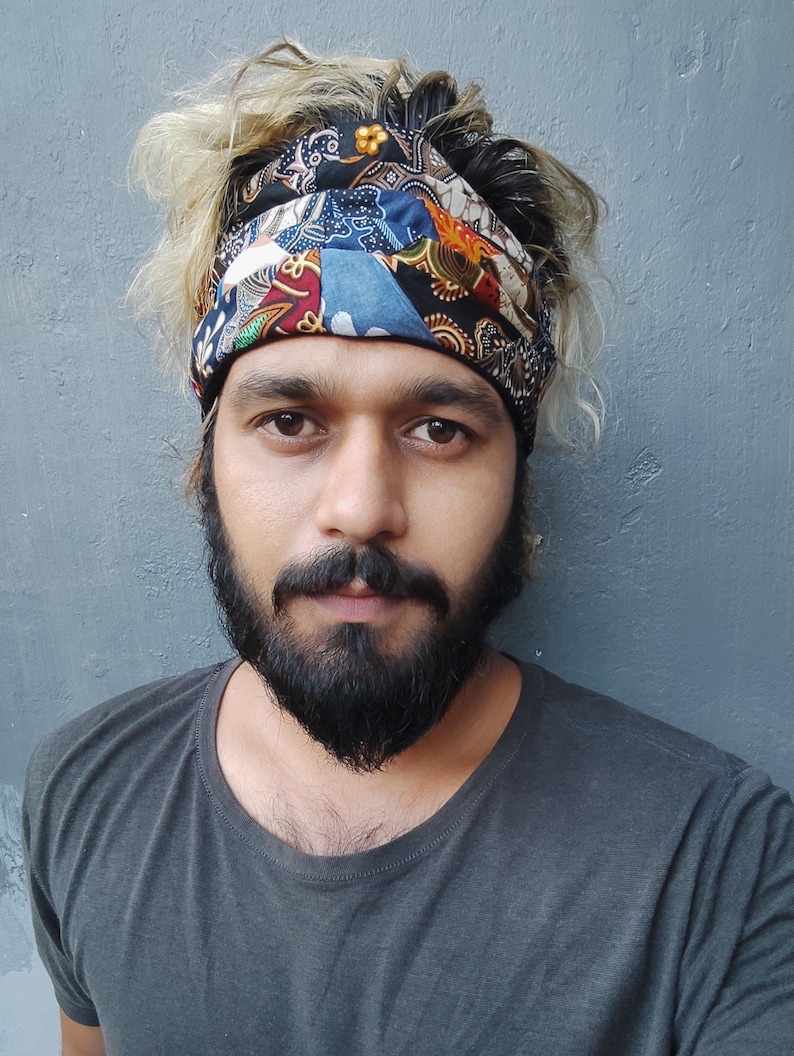 May include: A man with blonde hair and a beard is wearing a colorful patterned headband. He is wearing a dark grey t-shirt.
