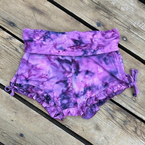 Puede incluir: Shorts de color morado con estampado tie-dye, dobladillo con volantes y un lazo en el lateral.