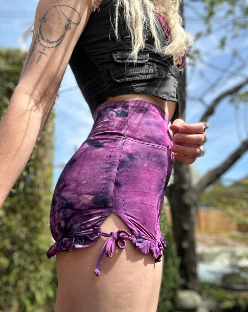 Puede incluir: Shorts de color morado con estampado tie-dye, dobladillo con volantes y un lazo en el lateral. Los shorts son de cintura alta y tienen un corte holgado.