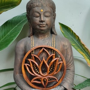 May include: A brown wooden statue of a meditating Buddha holding a round wooden carving of a lotus flower with gold accents.
