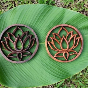 May include: Two wooden wall decor pieces with a carved lotus flower design. The pieces are circular and have a dark brown finish.