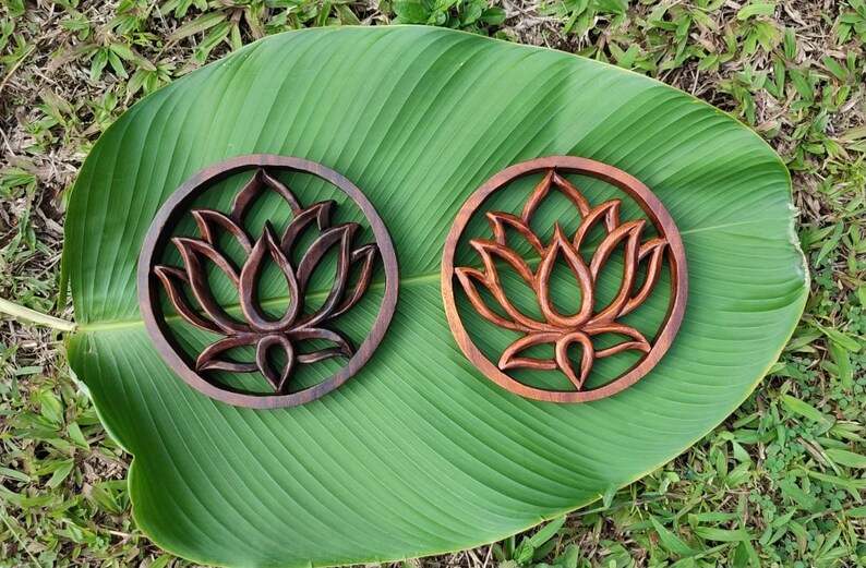 May include: Two wooden wall decor pieces with a carved lotus flower design. The pieces are circular and have a dark brown finish.